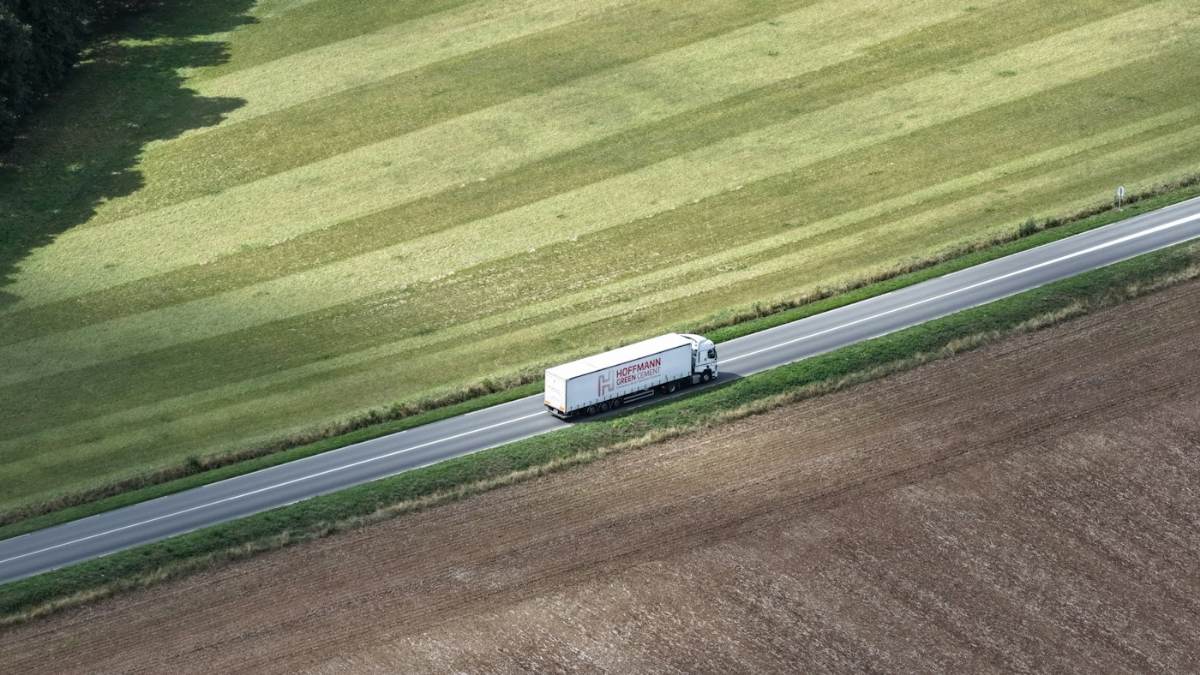 Caminhão branco em rodovia entre plantações, visto de cima